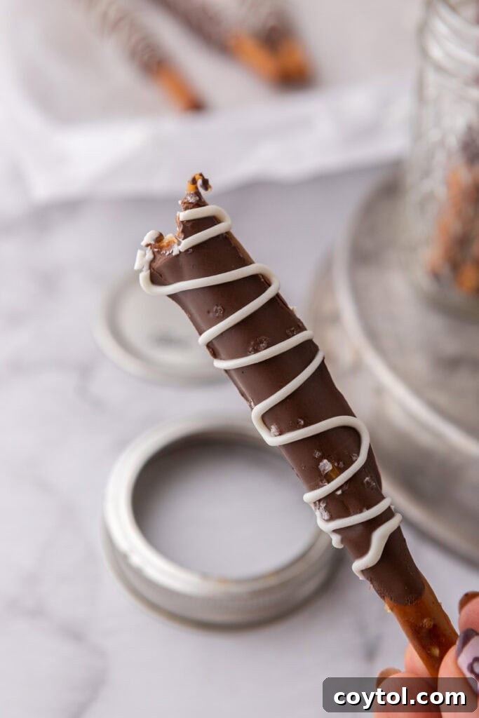 A close-up shot of a single caramel chocolate covered pretzel rod, perfectly coated and ready to be eaten.