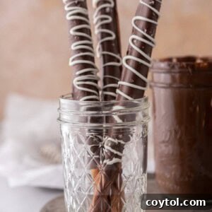 Three caramel chocolate covered pretzel rods in a cup, ready to be served.