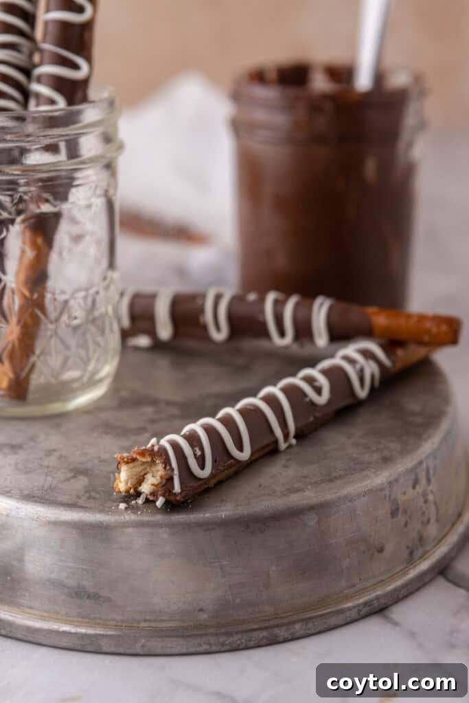 A close-up side shot of a single caramel chocolate covered pretzel rod, highlighting the distinct layers of crunchy pretzel, gooey caramel, and smooth chocolate, adorned with sea salt flakes.