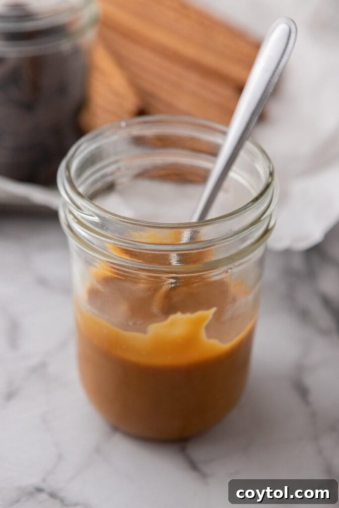 Melted caramel mixture being stirred in a cup with a spoon, showing its smooth consistency.