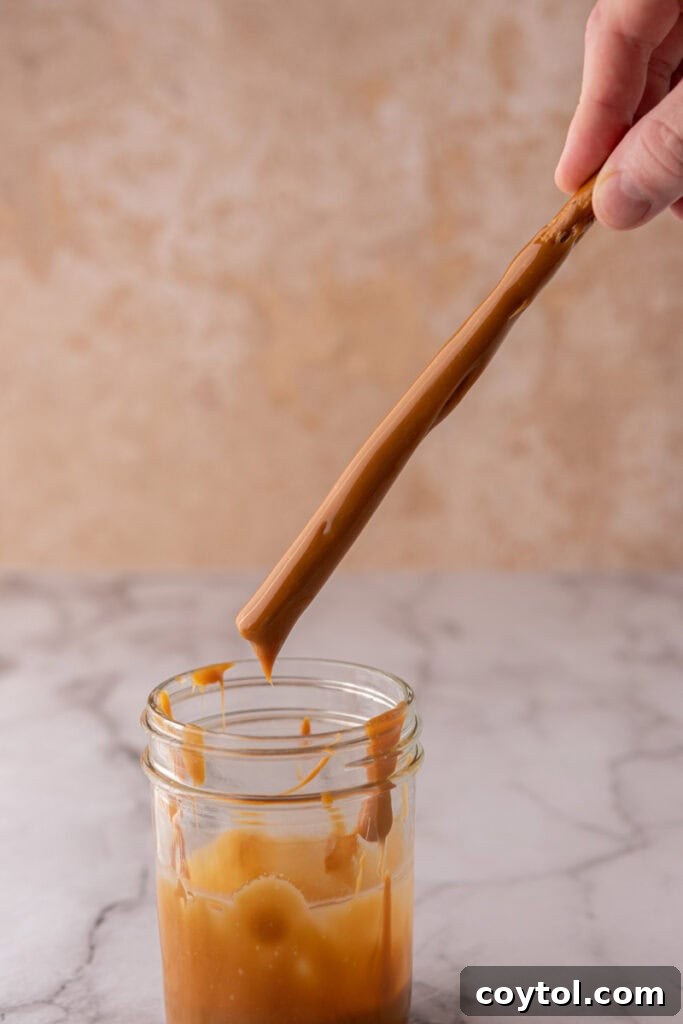 A pretzel rod being dipped into the melted caramel, showing the coating process.