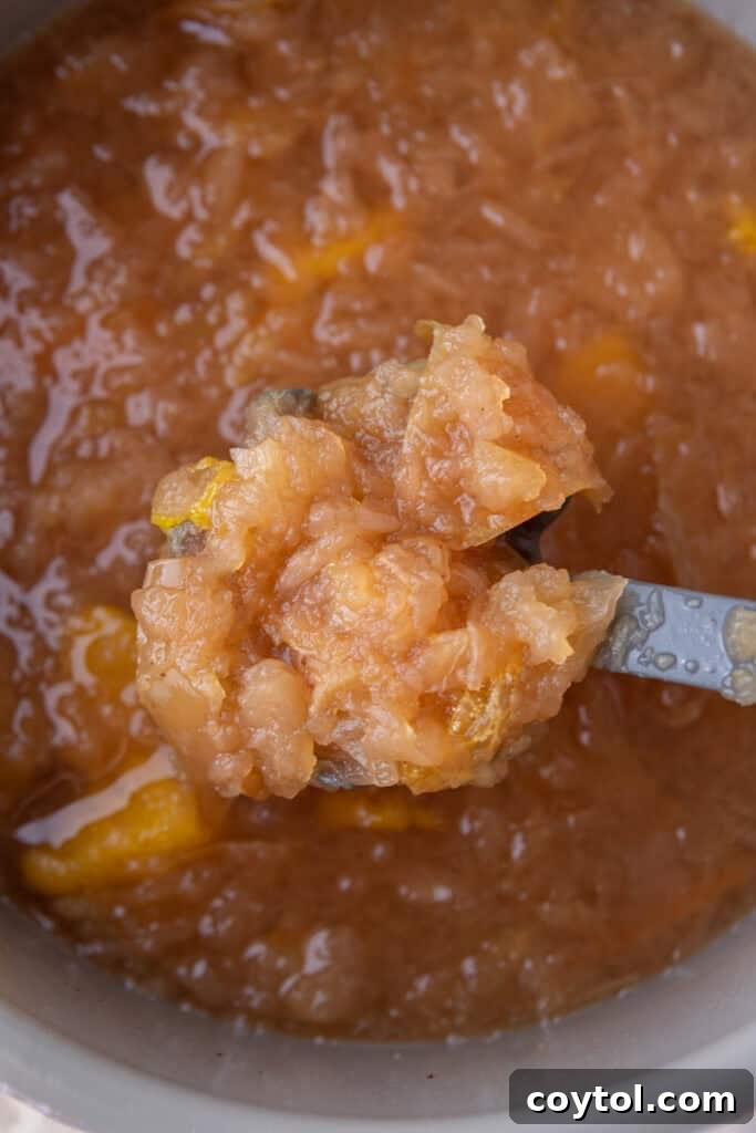 A potato masher crushing cooked apples and orange in an Instant Pot to extract maximum flavor for cider.