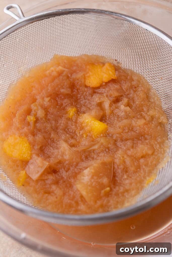 Straining mashed fruit mixture through a fine mesh strainer to produce clear Instant Pot apple cider.
