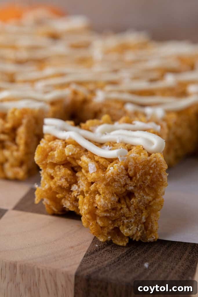 Autumn Pumpkin Rice Krispie Perfection 11 Close-up of a single pumpkin rice krispie treat, showing its texture and white chocolate drizzle.