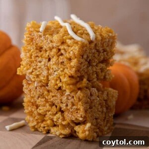 Pumpkin rice krispie treats with white chocolate drizzle on a stand