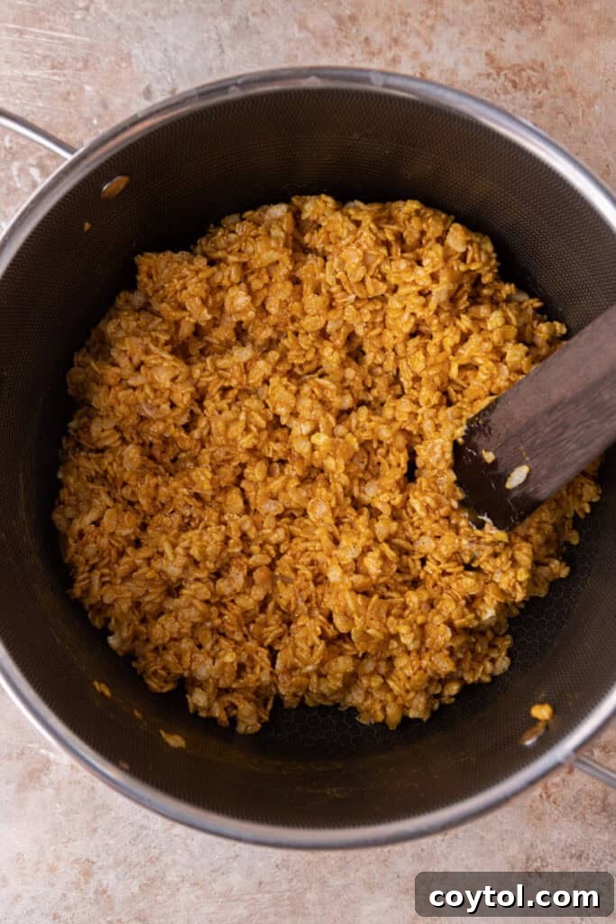 Autumn Pumpkin Rice Krispie Perfection 8 Rice Krispies cereal being folded into the pumpkin-marshmallow mixture in a pot.
