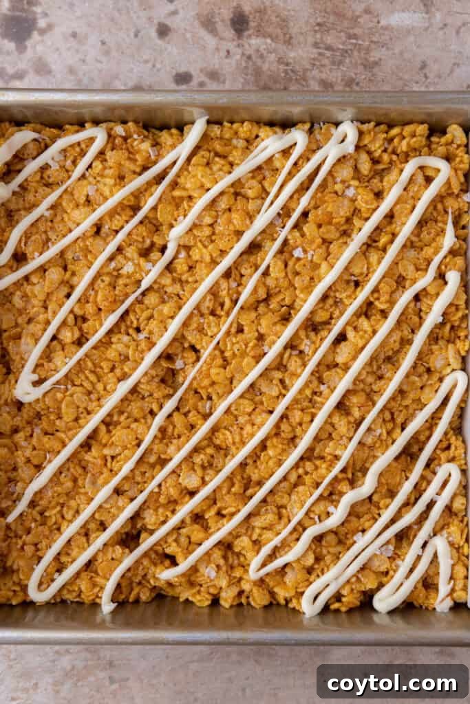 Autumn Pumpkin Rice Krispie Perfection 10 Pumpkin Rice Krispie treats in a pan with white chocolate drizzle on top.