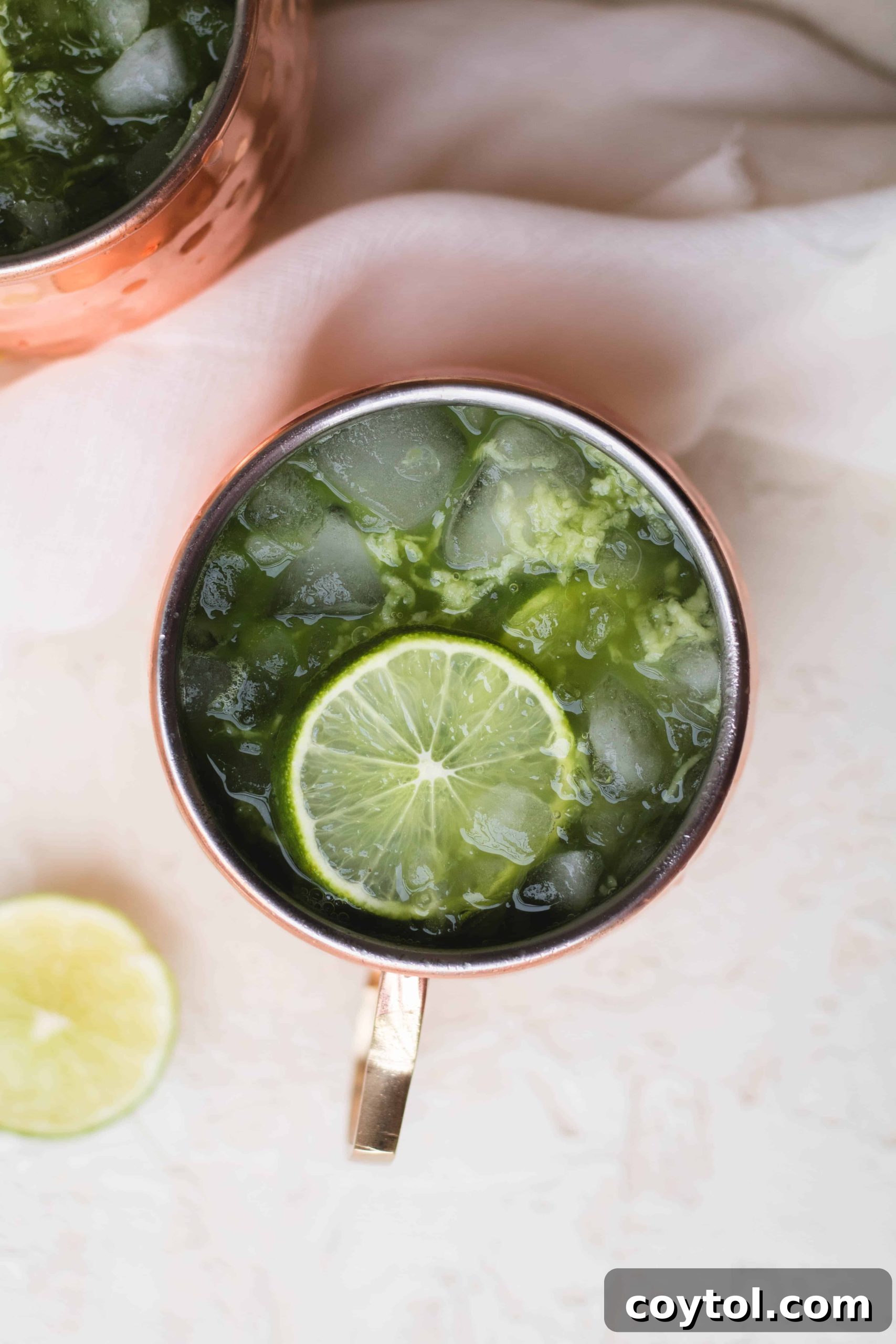 Close-up of a refreshing Virgin Matcha Moscow Mule in a copper mug, garnished with lime and fresh ginger