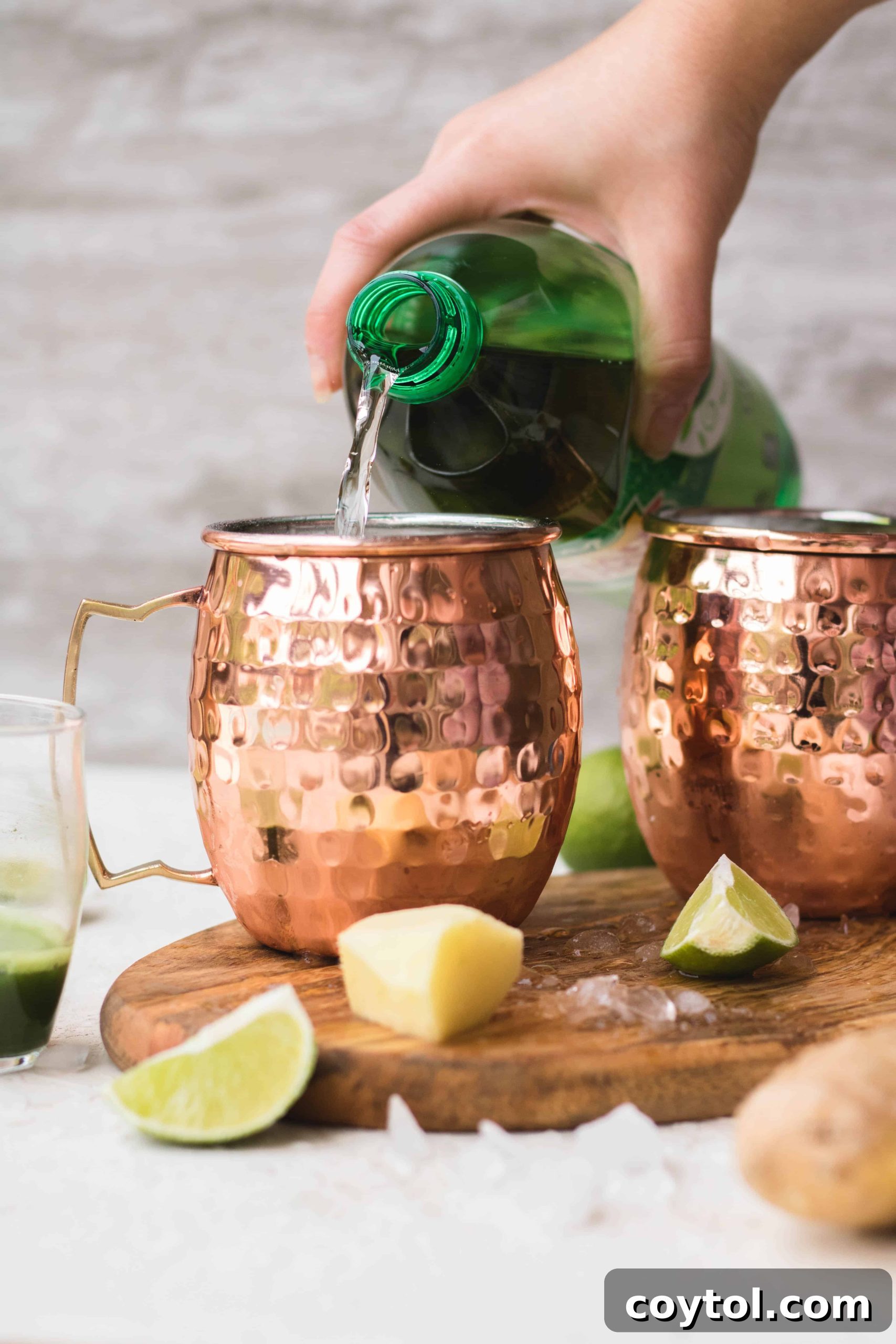 Pouring ginger ale into a copper Moscow Mule mug with ice and lime