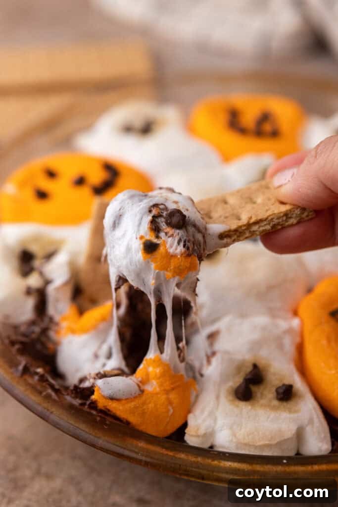 Wicked Good Halloween Smores Dip 2 Halloween S'mores Dip Recipe getting scooped up, showcasing melted chocolate and ghost marshmallows