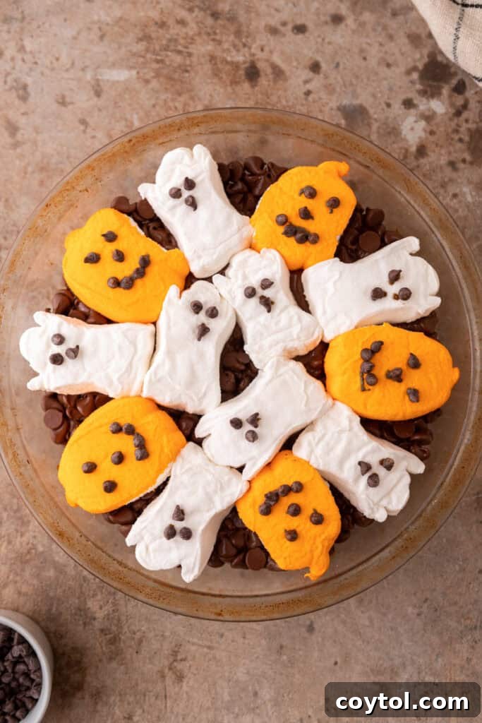 Wicked Good Halloween Smores Dip 6 chocolate chips in a baking dish with marshmallows on top before final bake