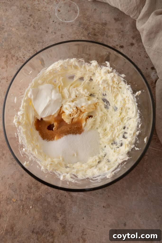 Bowl with unmixed cream cheese, sugar, and sour cream, ready for combining.
