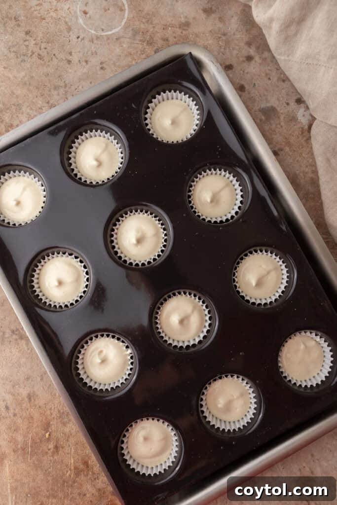 Raw cheesecake batter meticulously spooned into muffin tin liners over Nilla Wafers, ready for baking.