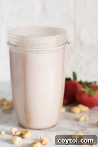 Strawberry cashew milk being strained through a nut milk bag