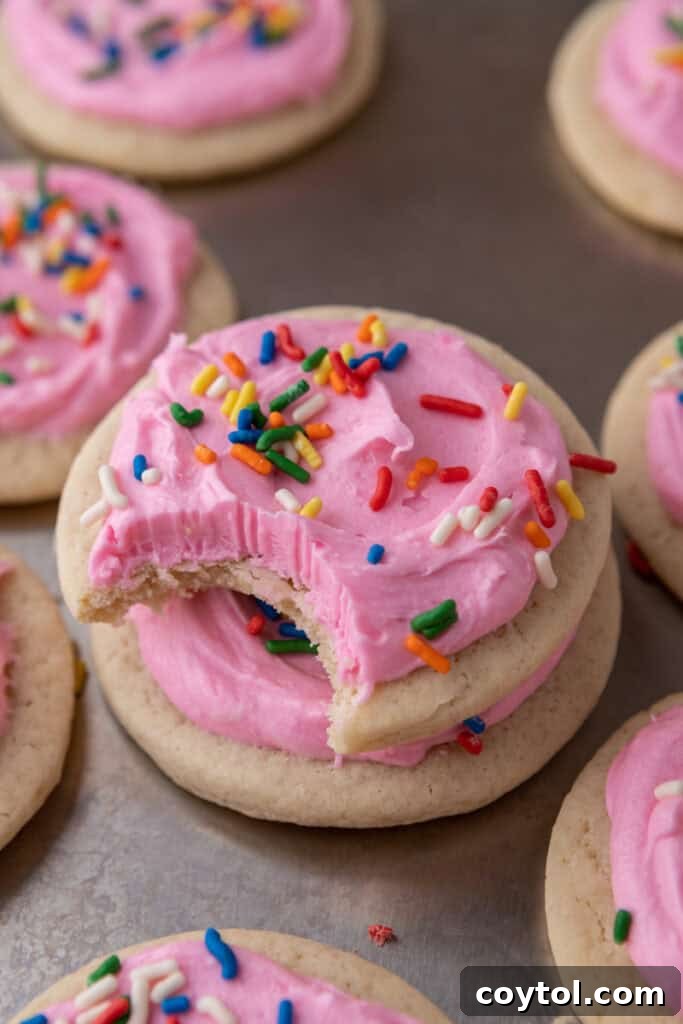 Pillowy Old-Fashioned Sour Cream Sugar Cookies 2 Soft sour cream sugar cookie with pink frosting and rainbow sprinkles, with a bite taken out to show the tender interior.