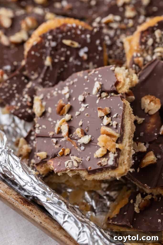 A perfectly portioned square of Ritz cracker Christmas crack, revealing the distinct layers of cracker, golden toffee, and smooth chocolate, with a hint of toppings.