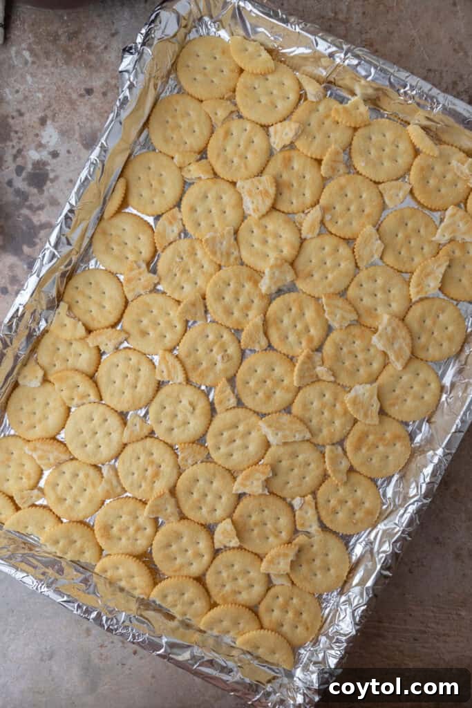Sheet pan lined with foil and a single layer of Ritz crackers ready to be coated in toffee, showing careful arrangement.