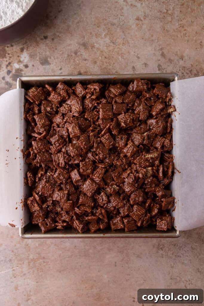 The coated Chex cereal mixture pressed firmly into a parchment-lined baking pan.