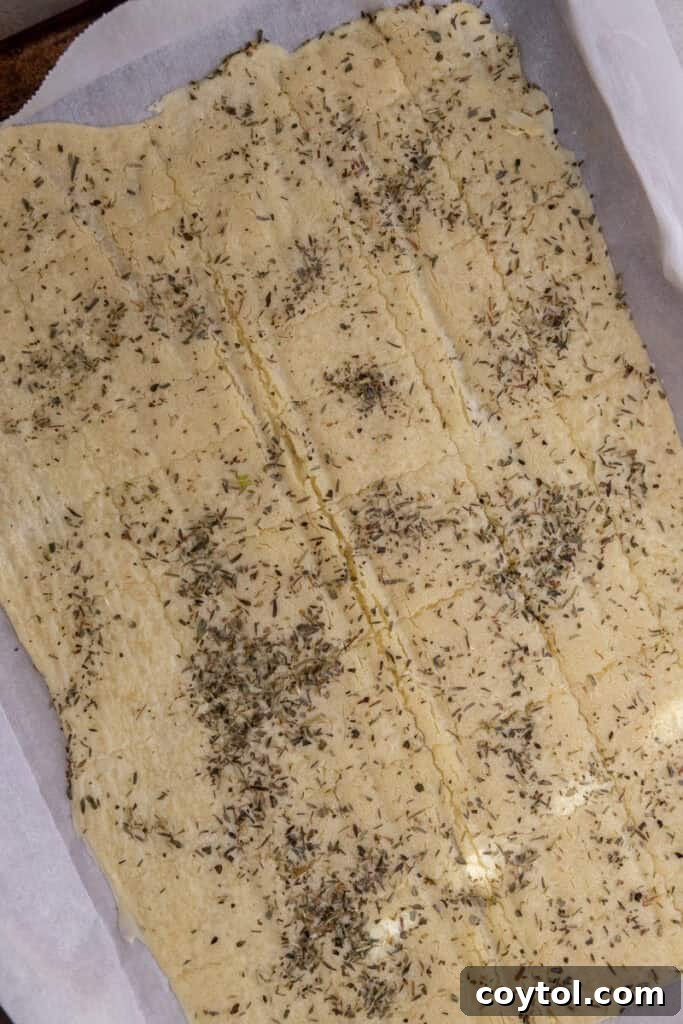 Seasoned sourdough discard dough with score marks on a baking sheet, pre-baking