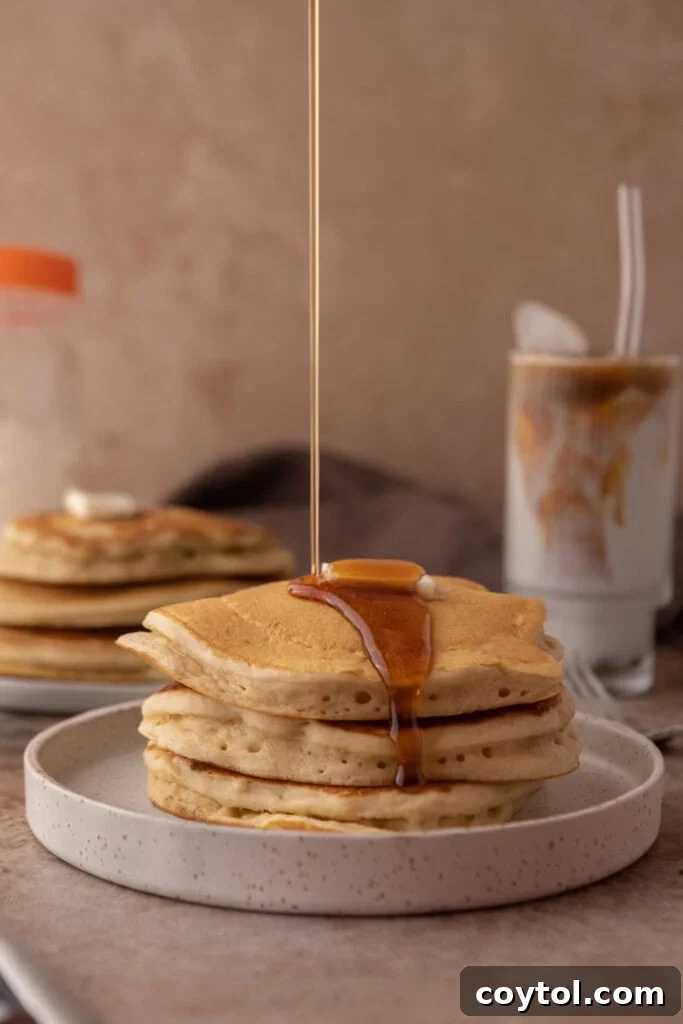 Side shot of a stack of fluffy Sourdough discard Pancakes with maple syrup cascading down.