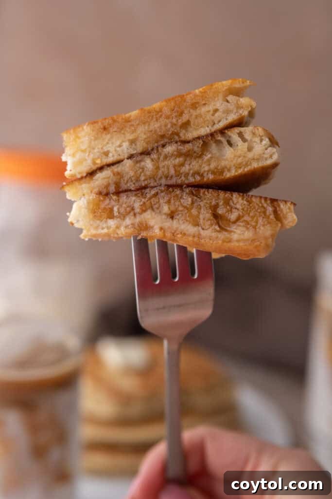A Sourdough discard Pancake on a fork, showing its fluffy texture and golden-brown exterior.