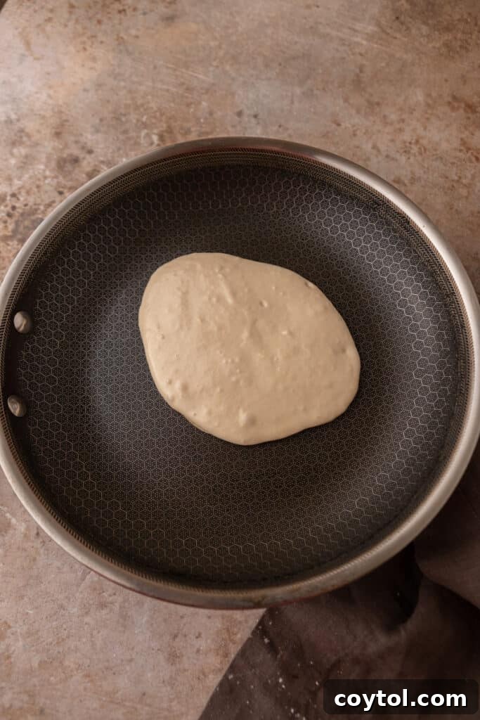 Sourdough discard pancake batter cooking on a hot skillet, showing bubbles forming on the surface.