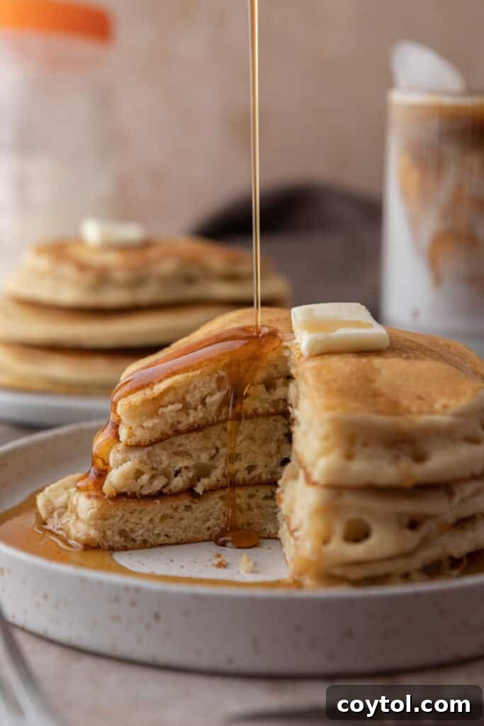 A close-up of a stack of Sourdough discard Pancakes on a plate, garnished with fresh berries and powdered sugar.
