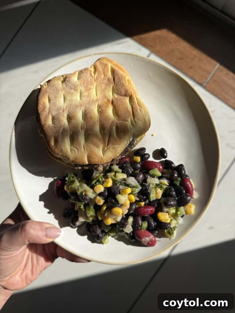 A perfectly cooked beef burger served on a plate alongside a fresh and colorful bean salad, showcasing a wholesome meal.