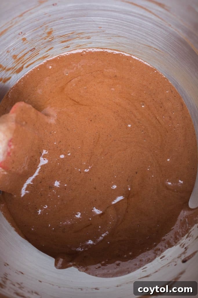 A spatula gently folding whipped aquafaba into melted chocolate in a glass bowl, showcasing the careful mixing process.