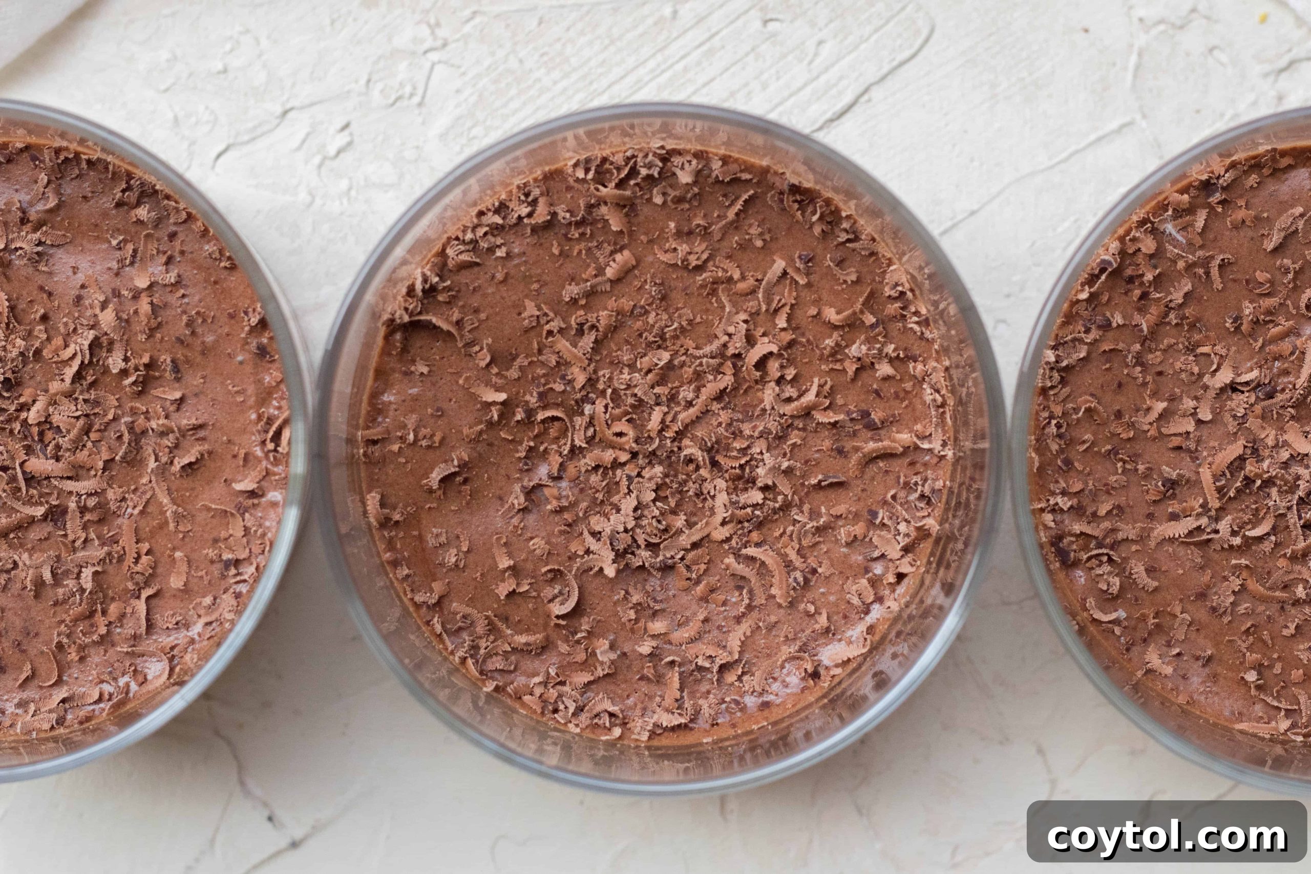 Three glass ramekins filled with smooth, dark vegan chocolate mousse, ready for chilling.