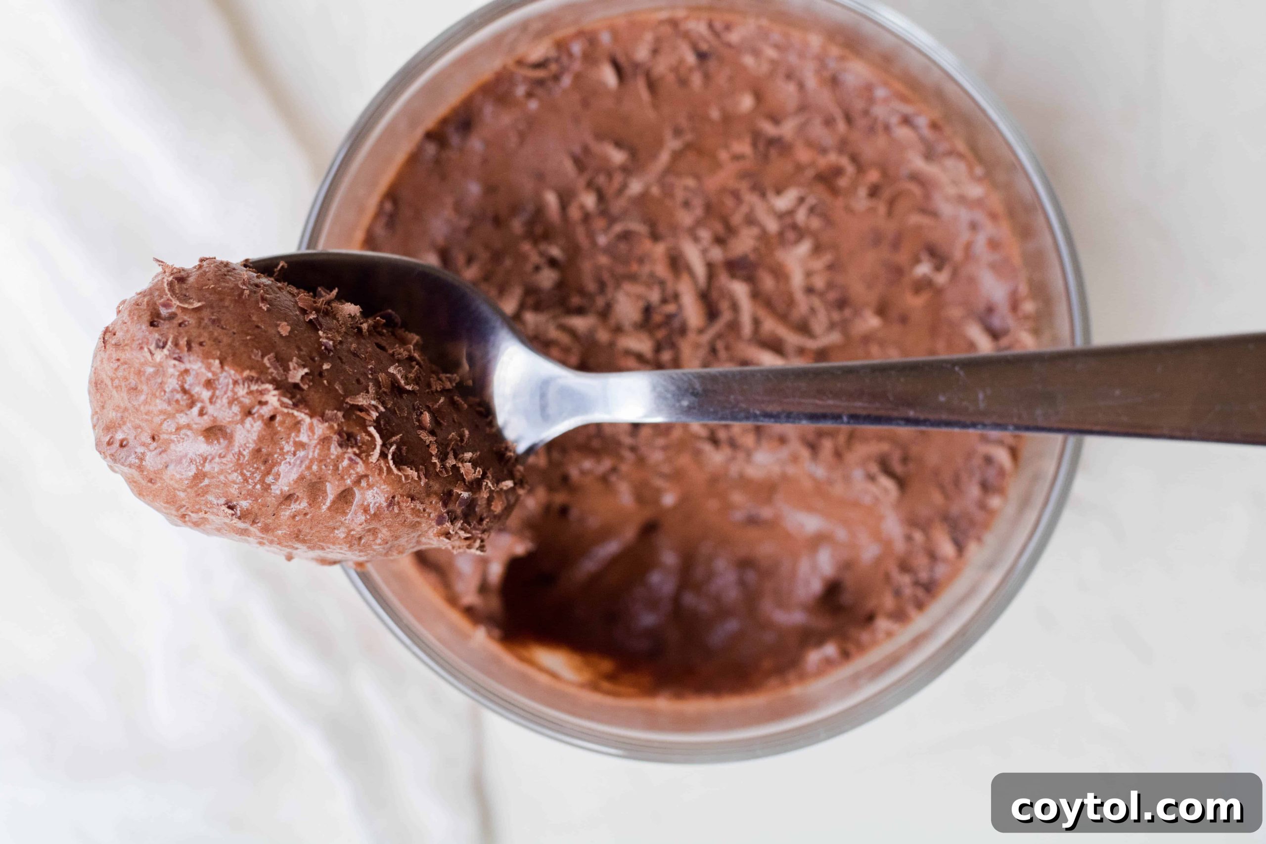 Vegan chocolate mousse with aquafaba, generously topped with chocolate shavings and fresh raspberries, presented in a small glass.