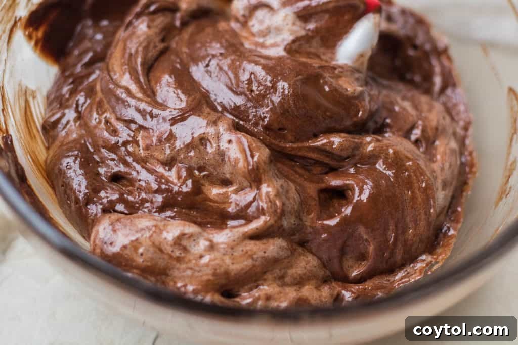 A stand mixer bowl with aquafaba being whipped into a white, foamy, meringue-like consistency.