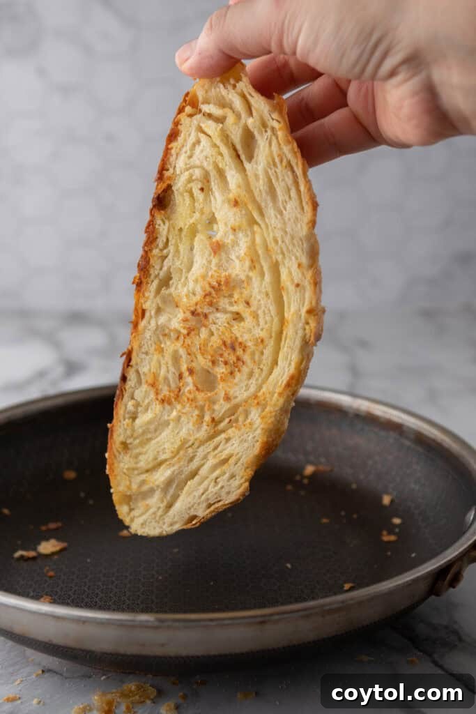 A golden-brown slice of Croissant Sourdough Bread being toasted, showcasing its beautiful, flaky layers and rich texture.