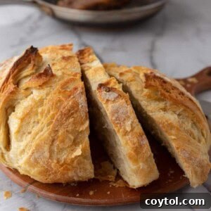 A round loaf of Sourdough Croissant Bread, beautifully sliced to reveal its rich, layered interior, displayed on a rustic cutting board.