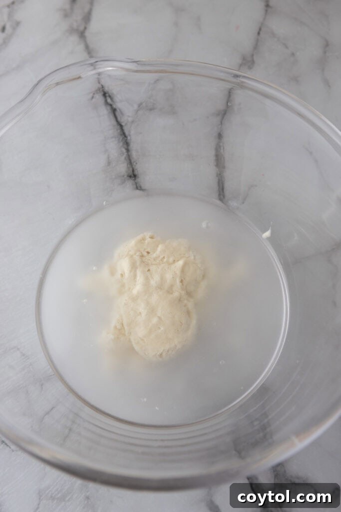 Sourdough starter and water being mixed together in a clear bowl, showing the initial hydration step.