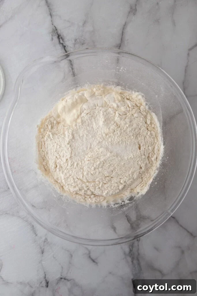 Flour, sourdough starter, and water combined in a bowl, forming a shaggy dough consistency before full incorporation.