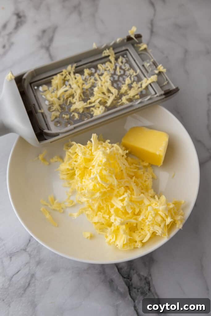 Cold butter being grated directly over the sourdough dough in a bowl, preparing for the lamination process.