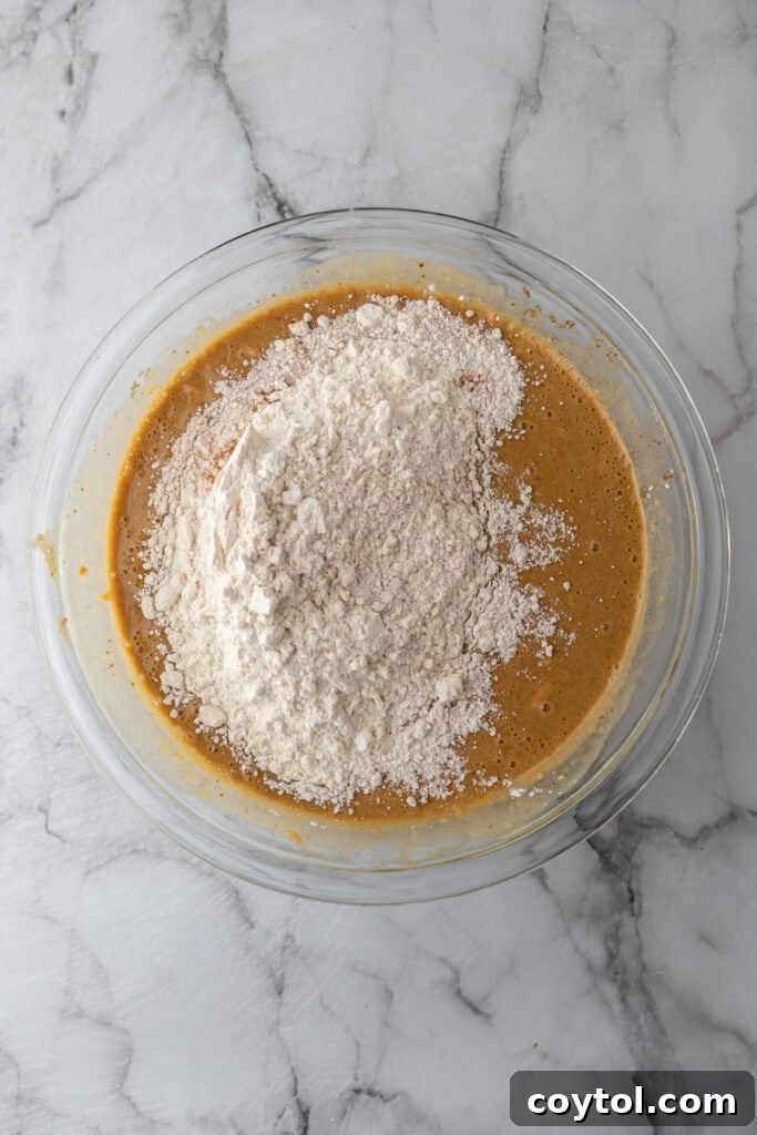 Dry ingredients being gradually added to the wet mixture in a bowl