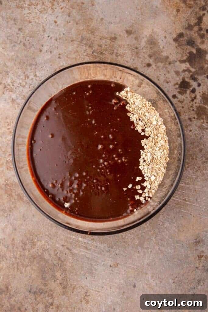 Quick oats being stirred into the hot chocolate and peanut butter mixture in a bowl, ensuring even coating.