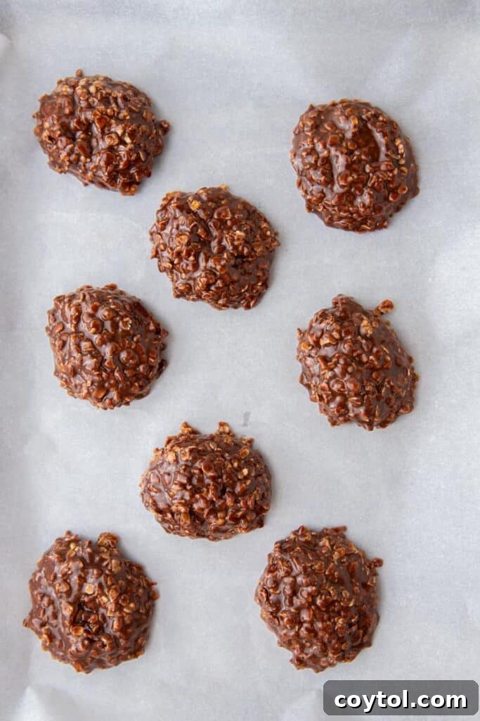 Freshly scooped no-bake chocolate oatmeal cookies cooling on a parchment-lined baking sheet.