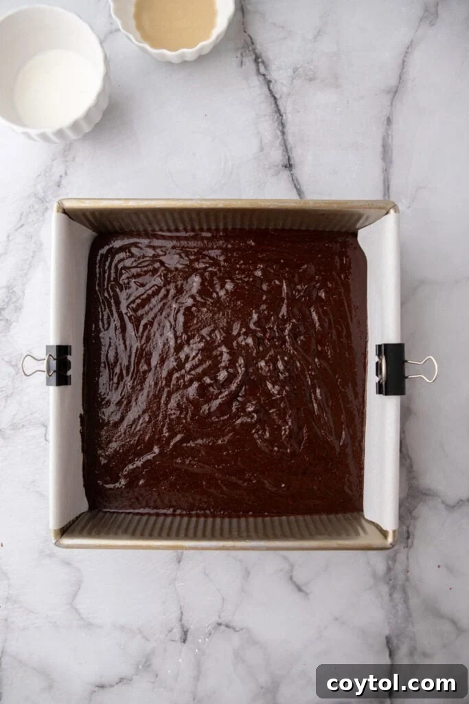 Unbaked brownie batter spread evenly in a parchment-lined baking pan.