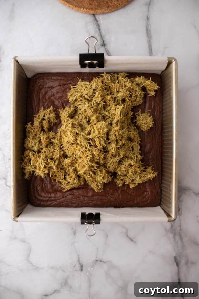 Pistachio kataifi filling being spread over the cooled brownie layer.