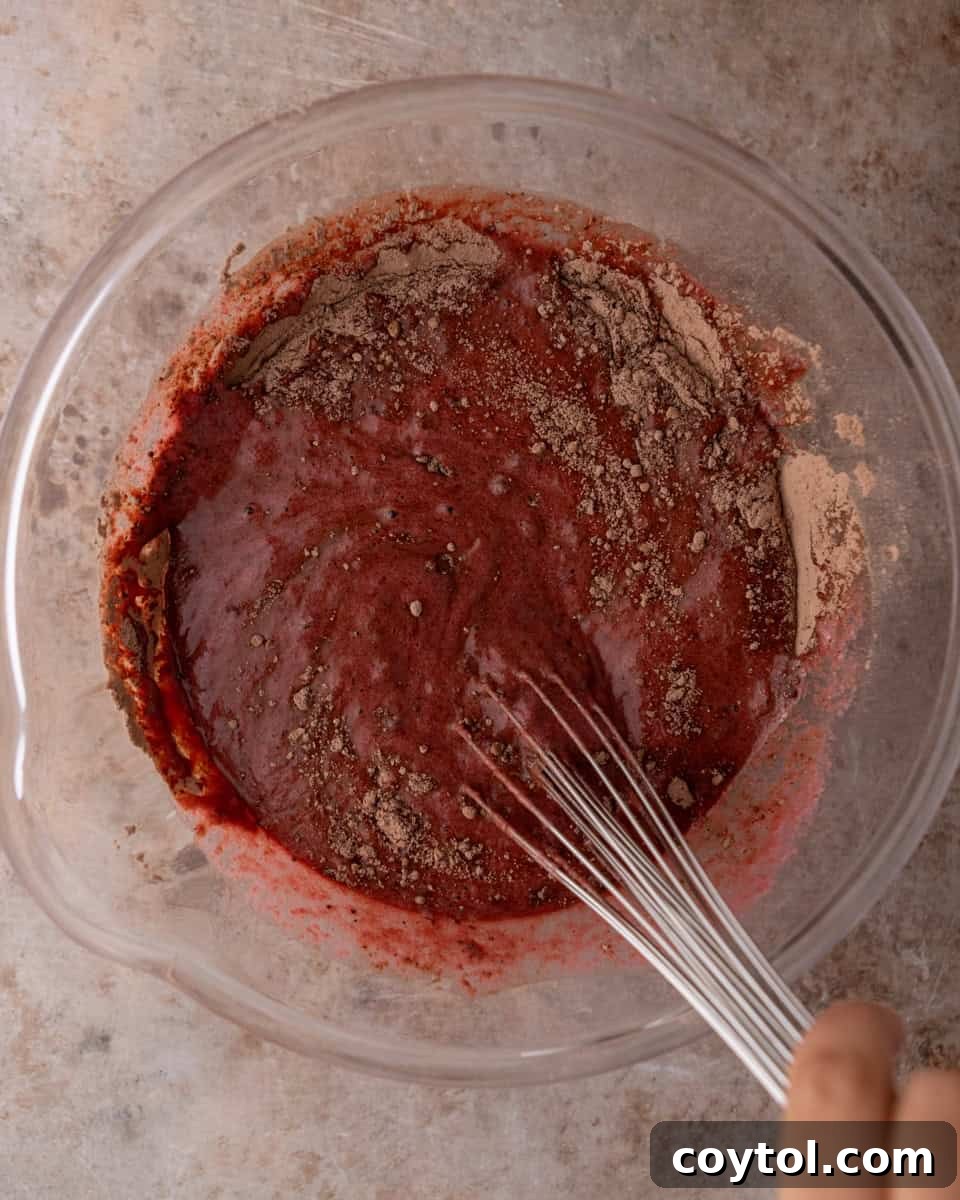 Dry chocolate cake ingredients being added to beet mixture in a bowl