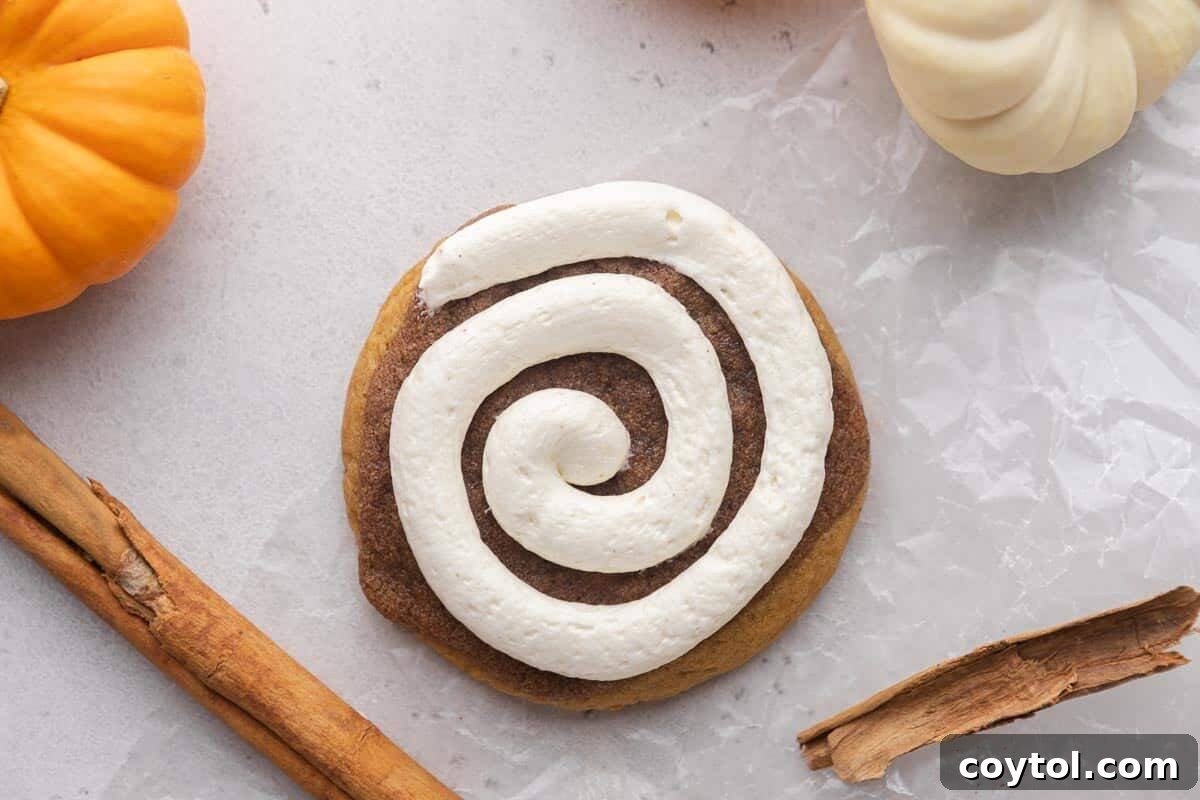 Crumbl pumpkin roll cookie with cream cheese frosting and mini pumpkins