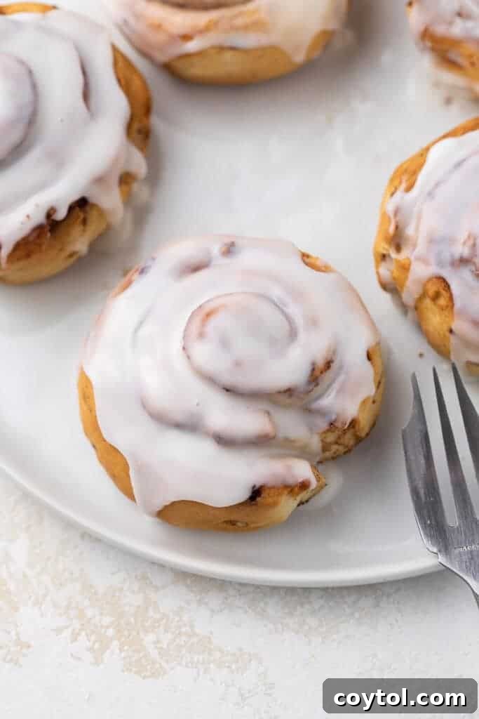 Air fryer cinnamon rolls topped with a gooey glaze on a while plate