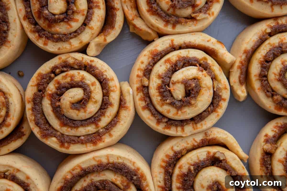 Twelve unbaked carrot cake cinnamon rolls arranged in a baking pan showing the swirl pattern before rising

