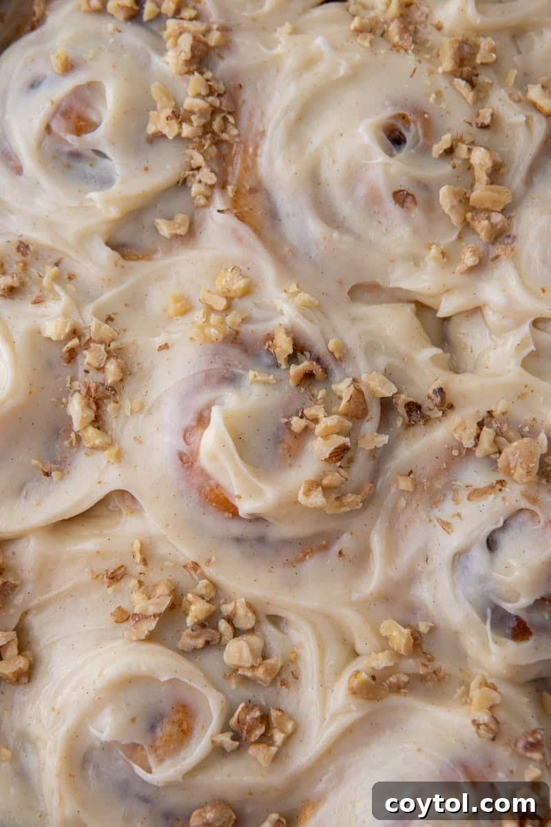 Close-up overhead of carrot cake cinnamon rolls covered in brown butter cream cheese frosting and topped with chopped walnuts