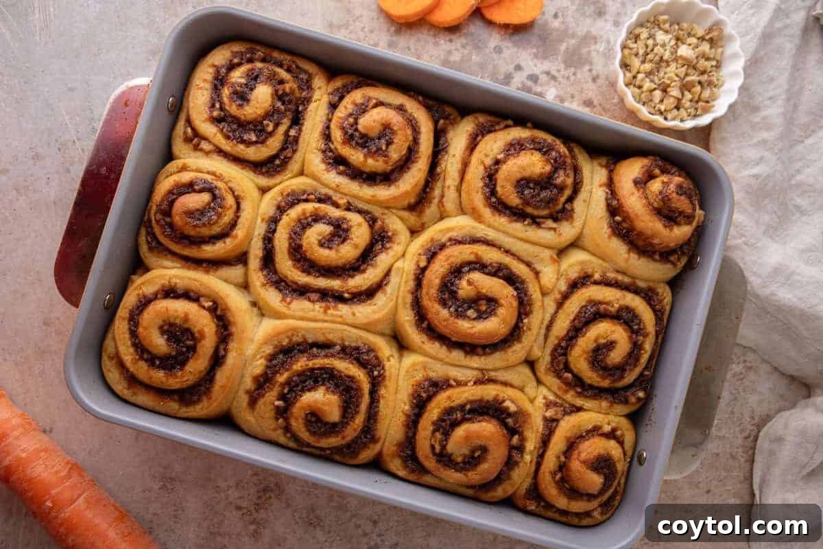 Twelve freshly baked rolls in a 9x13 baking pan with golden tops and visible cinnamon swirls, unfrosted