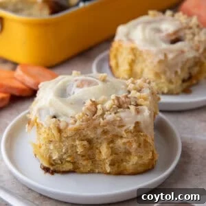 Two carrot cake cinnamon rolls with brown butter cream cheese frosting and chopped walnuts on white plates with a yellow baking pan in the background