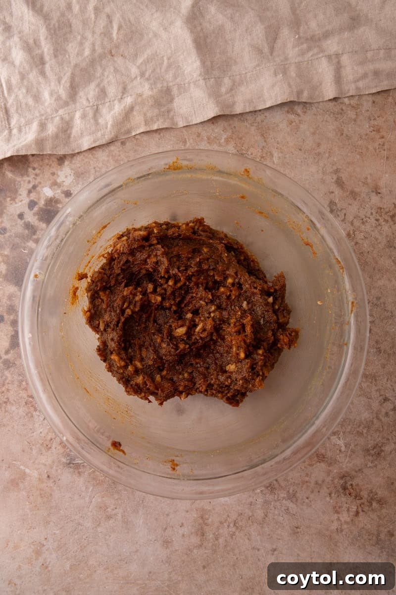 Carrot cake cinnamon roll filling mixed together in a glass bowl, showing a thick dark brown paste with walnut pieces